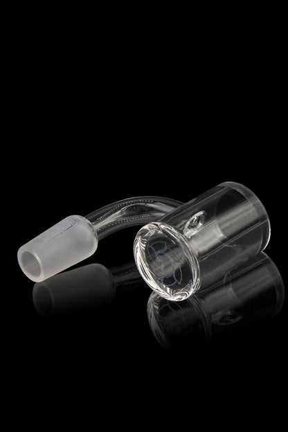 Clear glass cannabis oil rig with a bent neck and spherical attachment, displayed on a reflective surface against a black background.