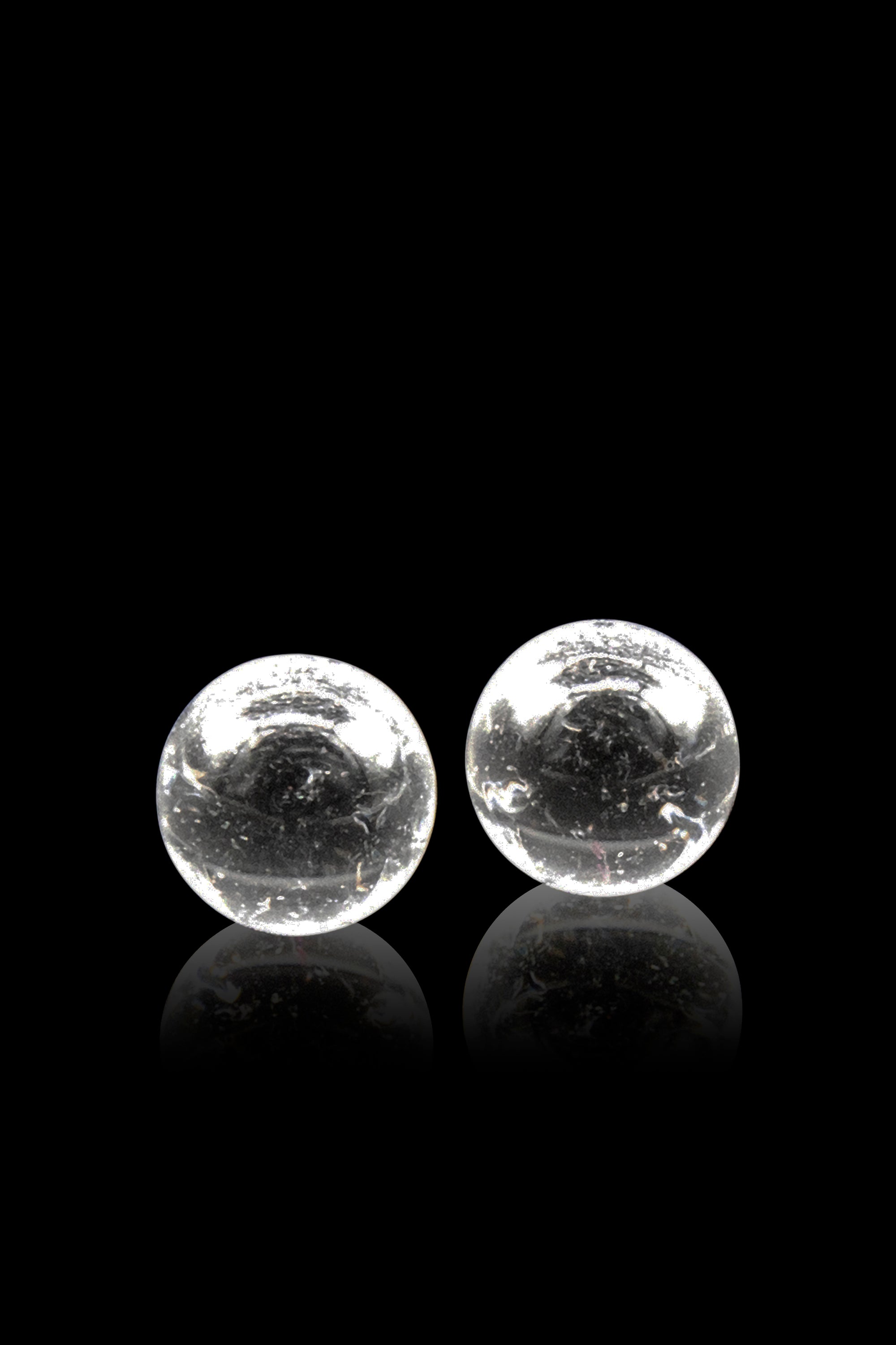 Two clear glass marbles with internal bubbles rest on a reflective black surface.
