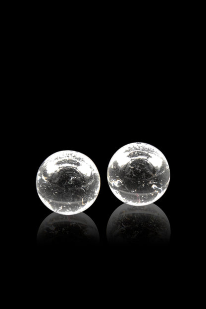 Two clear glass marbles with internal bubbles rest on a reflective black surface.