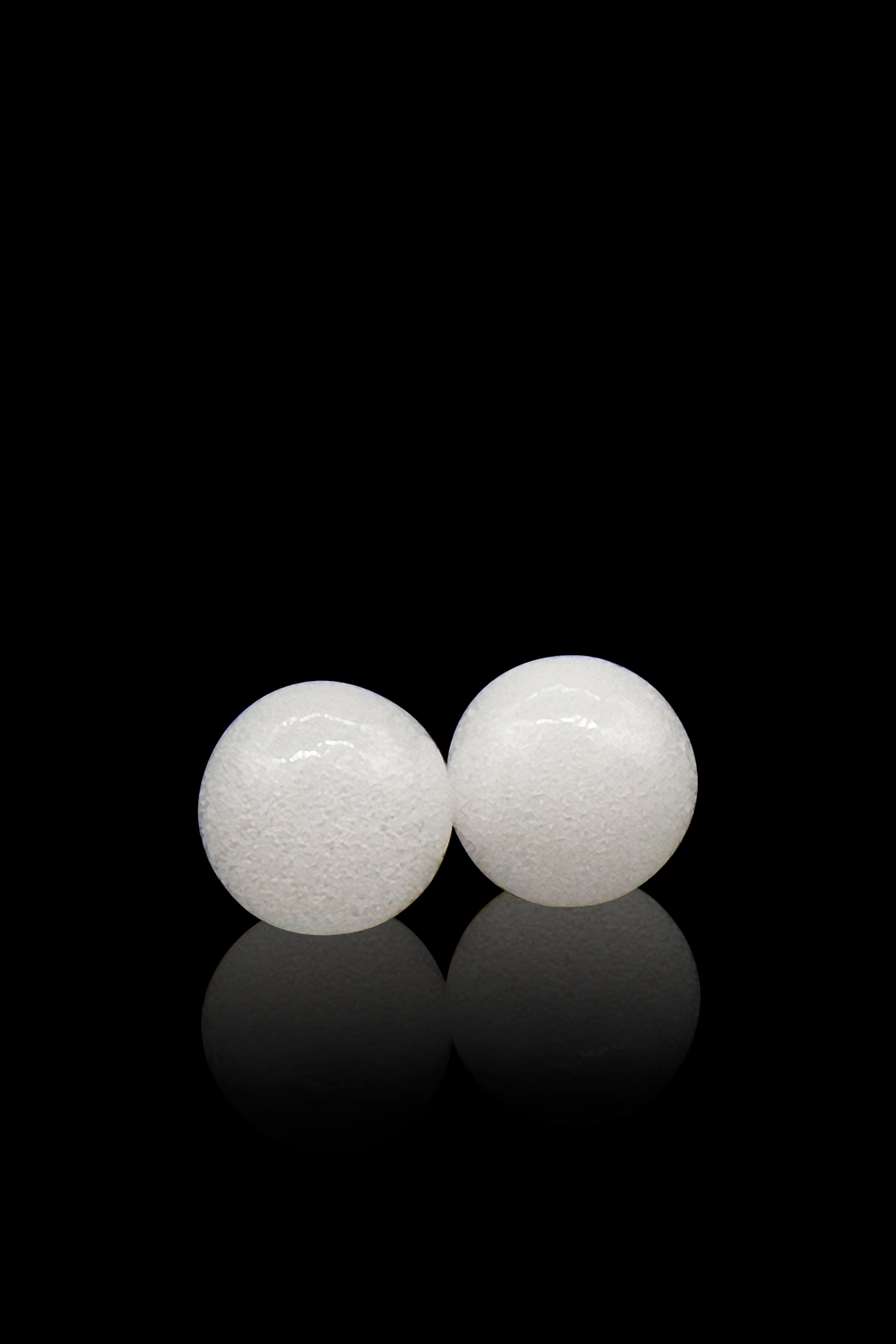 Two white, spherical cannabis vaporization tablets with reflections on a black background.