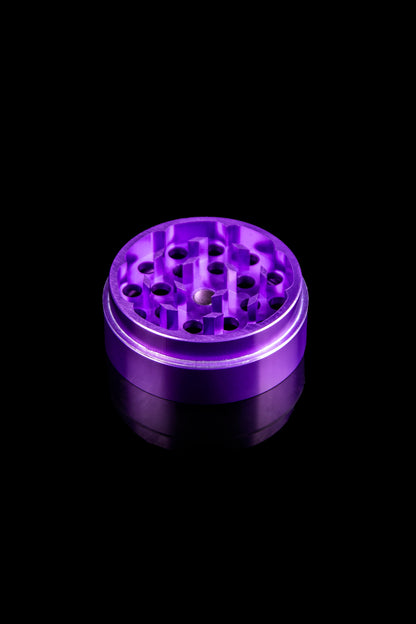Purple cannabis grinder on a black reflective surface.