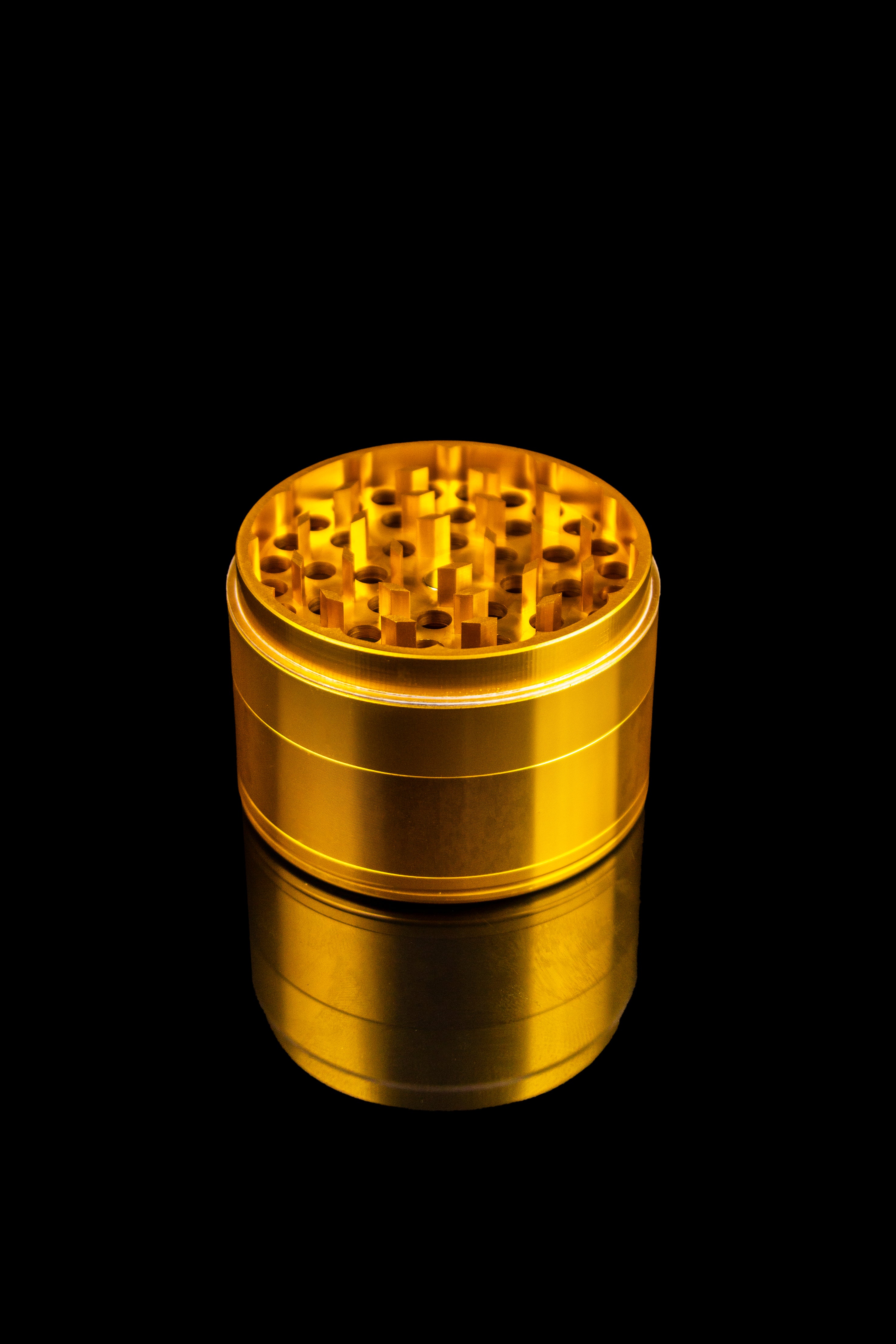 Gold cannabis grinder against a black background.