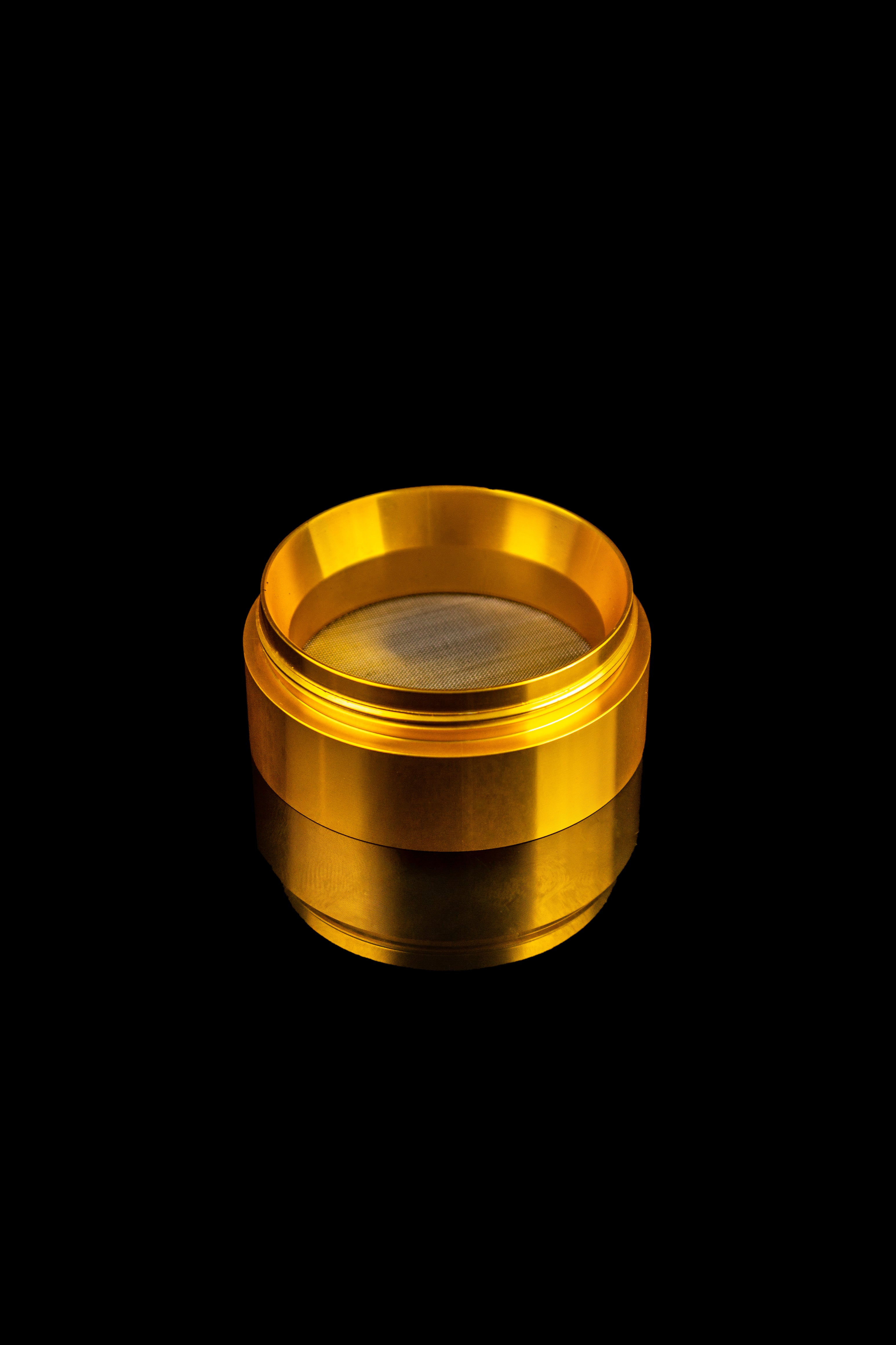 Gold-toned cannabis grinder with a mesh screen.