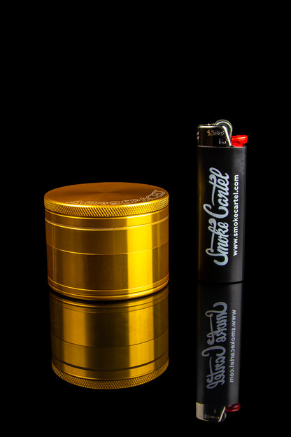 Gold cannabis grinder and black lighter with "Smoke Cartel" branding against a dark background.