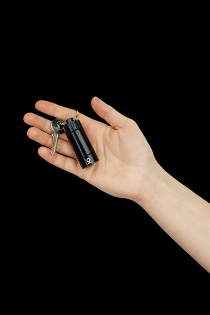 Hand holding a sleek, black cannabis oil vape pen with keys attached against a dark background.