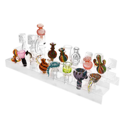 A front view of the Banger & Bowl Clear Acrylic Display Holder, showcasing an arrangement of clear glass pieces on a transparent tiered stand.