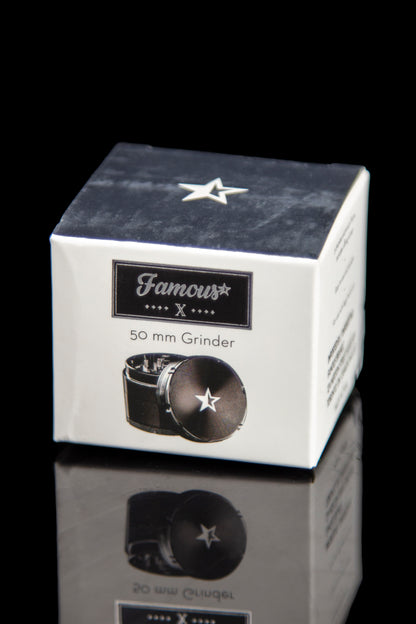 A close-up, angled view of the silver Famous X 4-Piece Grinder reflecting on a shiny black surface.