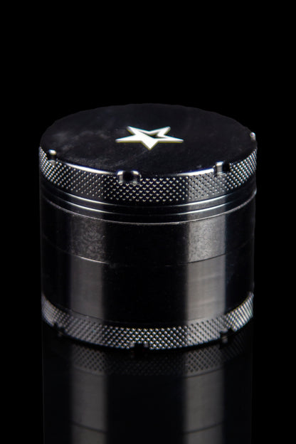 A close-up, angled view of the Famous X 4-Piece Grinder, showcasing its metallic, multi-tiered design against a dark background.