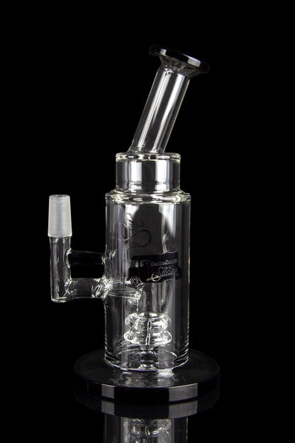 Clear glass water pipe (rig) with intricate bubbler design, reflecting on a glossy black surface.