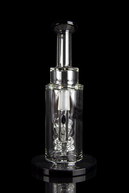 Clear glass oil rig with intricate bubbler design, displayed on a reflective surface against a black background.