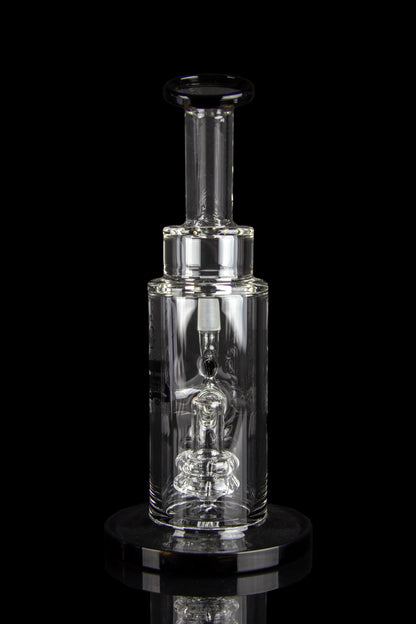 Clear glass dab rig with intricate percolator and vapor pathway, displayed on a reflective surface.
