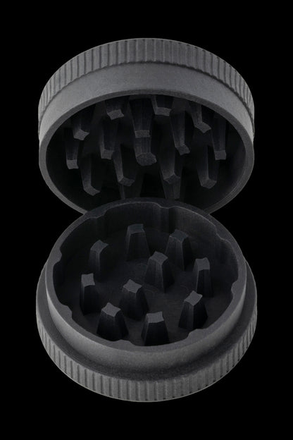 Open metal cannabis grinder with visible grinding teeth, against a black background.