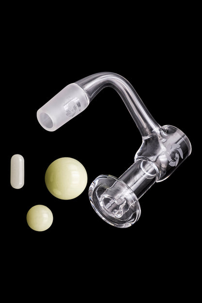 Clear glass dab rig with quartz insert and cannabis concentrates floating nearby on a black background.