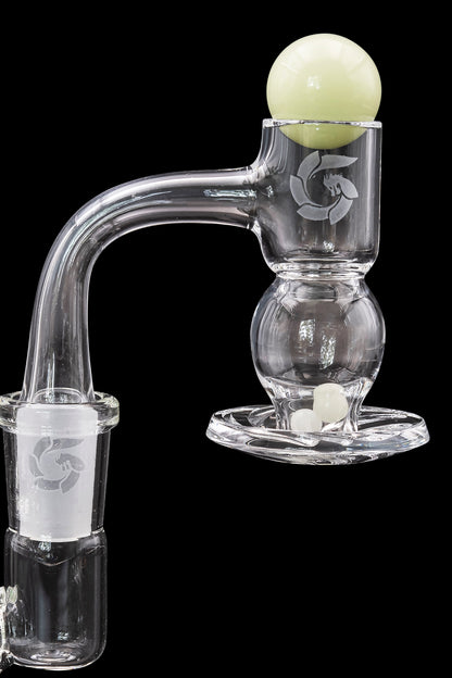 Clear glass dab rig with etched logo and spherical bubbler, alongside white carb caps.
