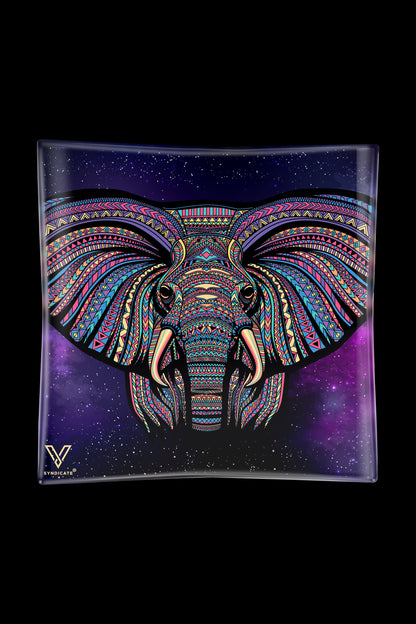 A vibrant, patterned elephant head design on a glass tray with a starry purple background, branded with a cannabis accessory company logo.
