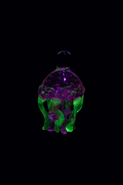 A vibrant, angled view of the Empire Glassworks UV Jellyfish Carb Cap, displaying a translucent, jellyfish-like form with glowing purple and green hues.