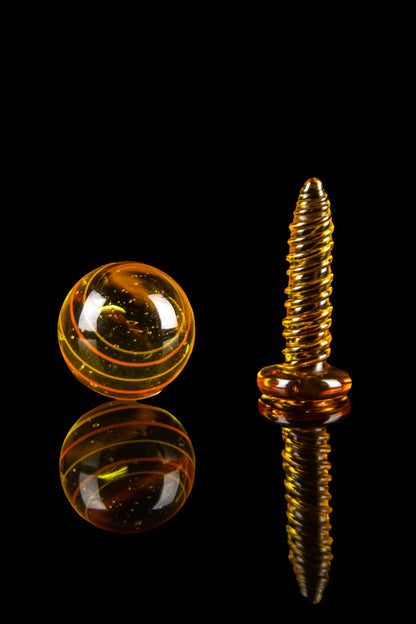 Amber glass cannabis marble and oil dome with reflective surface on black background.