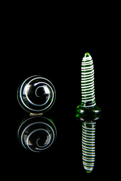 Green and clear glass cannabis oil burner and spiral marble against a black reflective surface.
