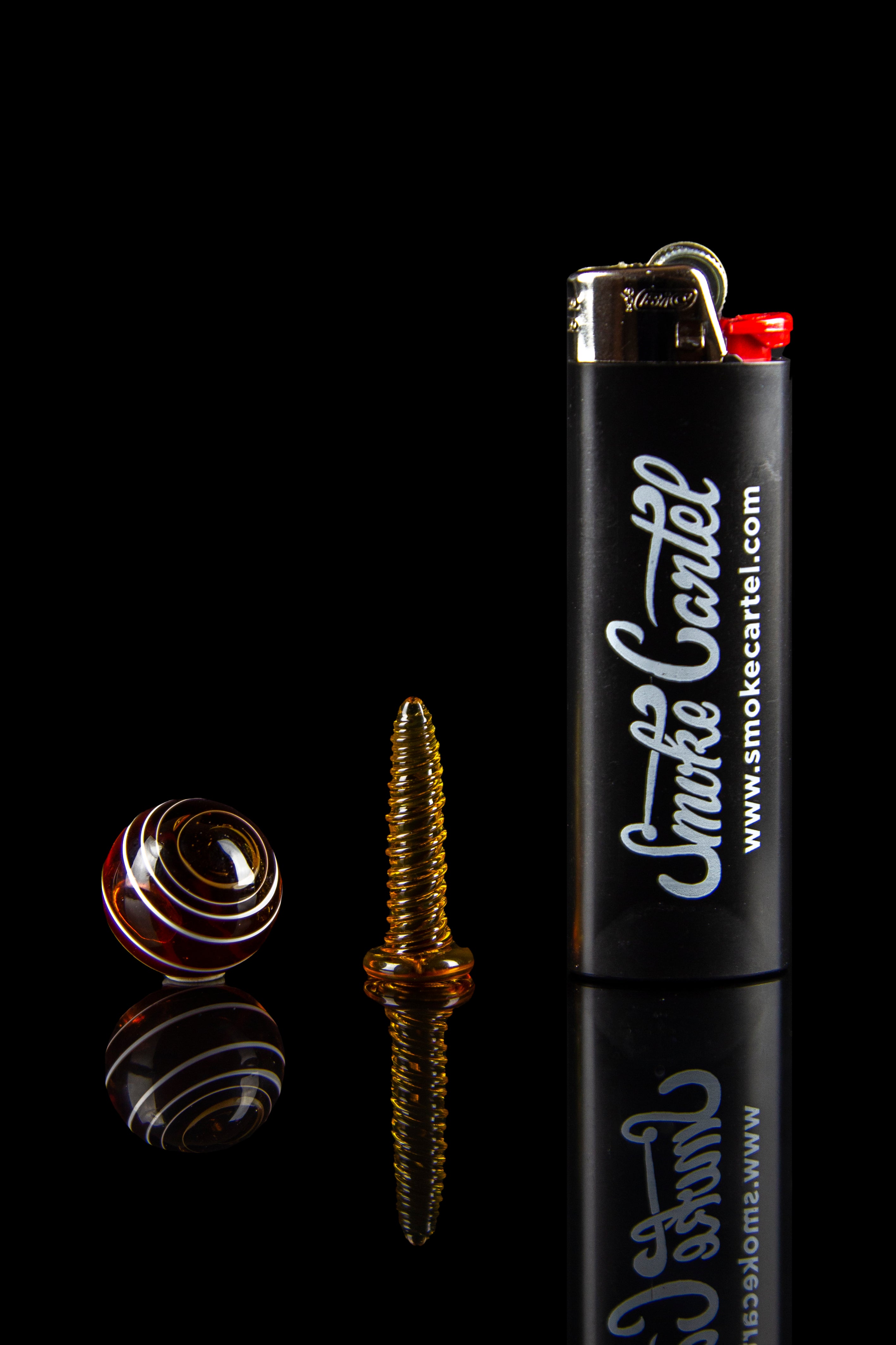 A studio shot of cannabis accessories: a glass bubbler, a metal coil, and a branded lighter with reflective surface."
