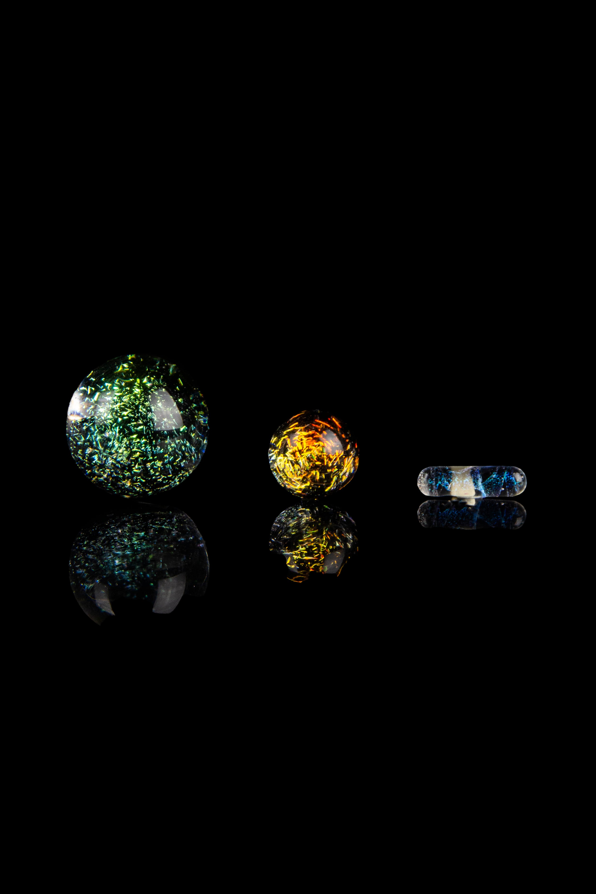 Colorful glass marbles and capsules against a black background, likely cannabis accessories.