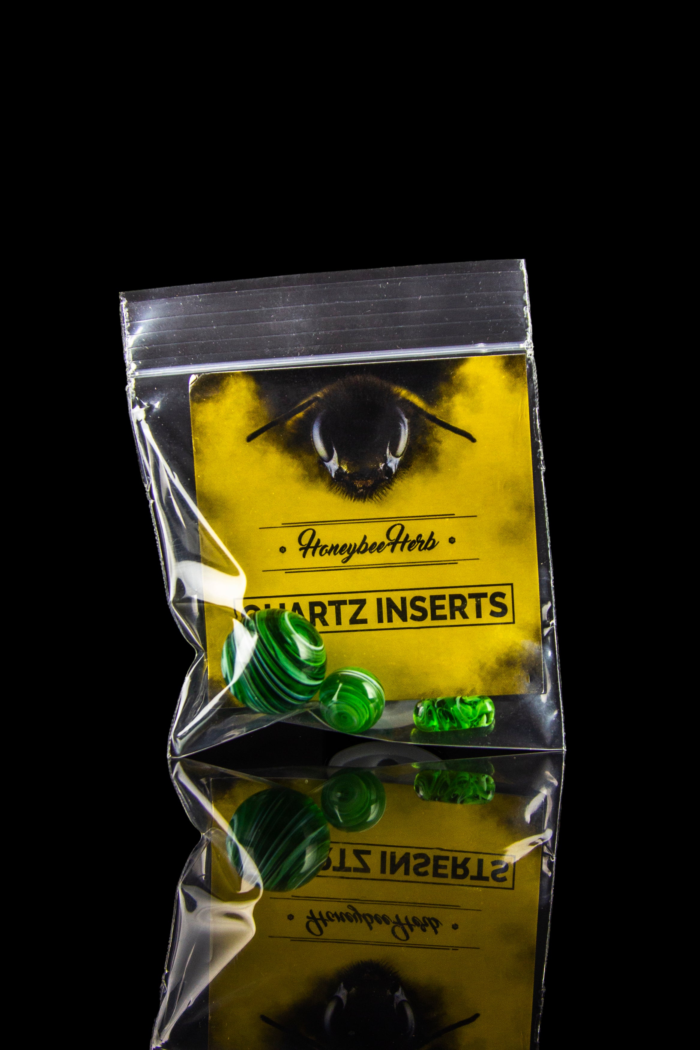Clear plastic bag containing green quartz inserts for cannabis concentrates, branded with "Honeybee Herb" and an eye illustration, against a black background.