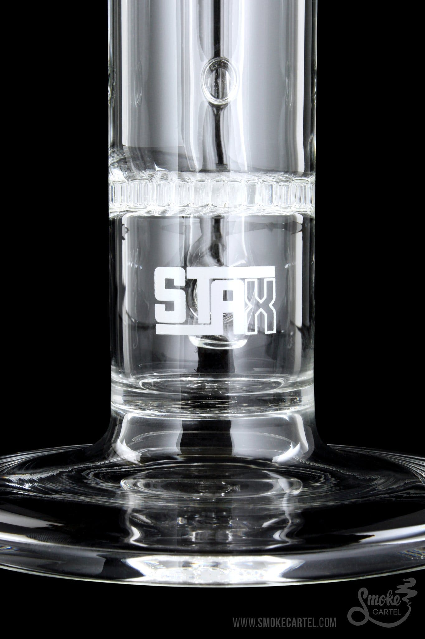 Close-up of a clear glass water pipe with “STAX” etched on the side, filled with water and reflecting on a dark surface.