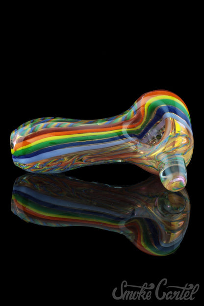 A side view of the Heavy Cane Worked Rainbow Spoon - Rainbow Mega Pipe shows colorful glasswork reflected on a dark surface.