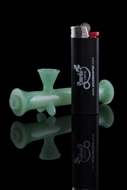 Green glass dab rig and black lighter with cannabis-themed branding, reflected on a black surface.
