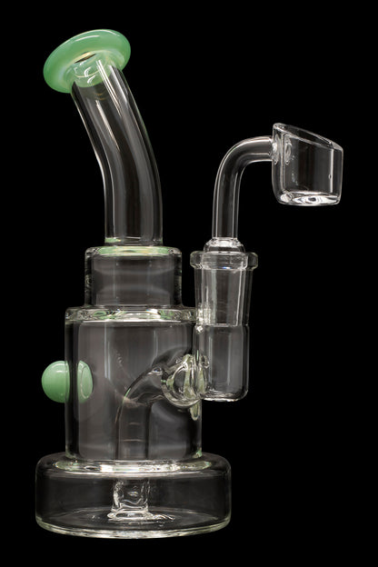 Clear glass dab rig with green accents and a quartz banger.