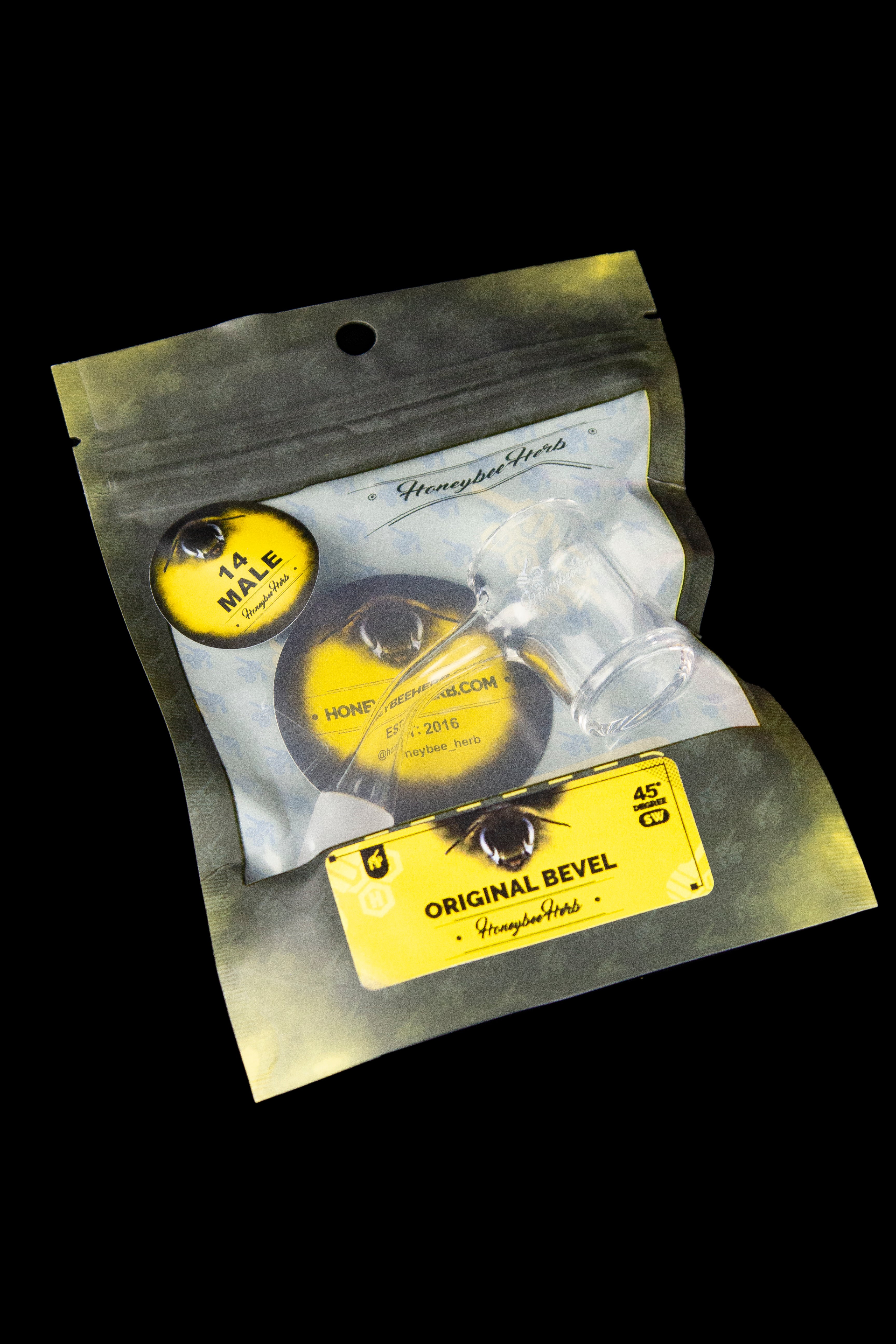 A sealed, translucent gold mylar bag labeled “Honeybee Herbs” containing a small, round sticker with an eye design and the text “14 Male.”