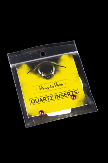 A sealed plastic bag containing "HoneybeeHerb" branded quartz inserts for use with cannabis concentrates, displayed against a black background.