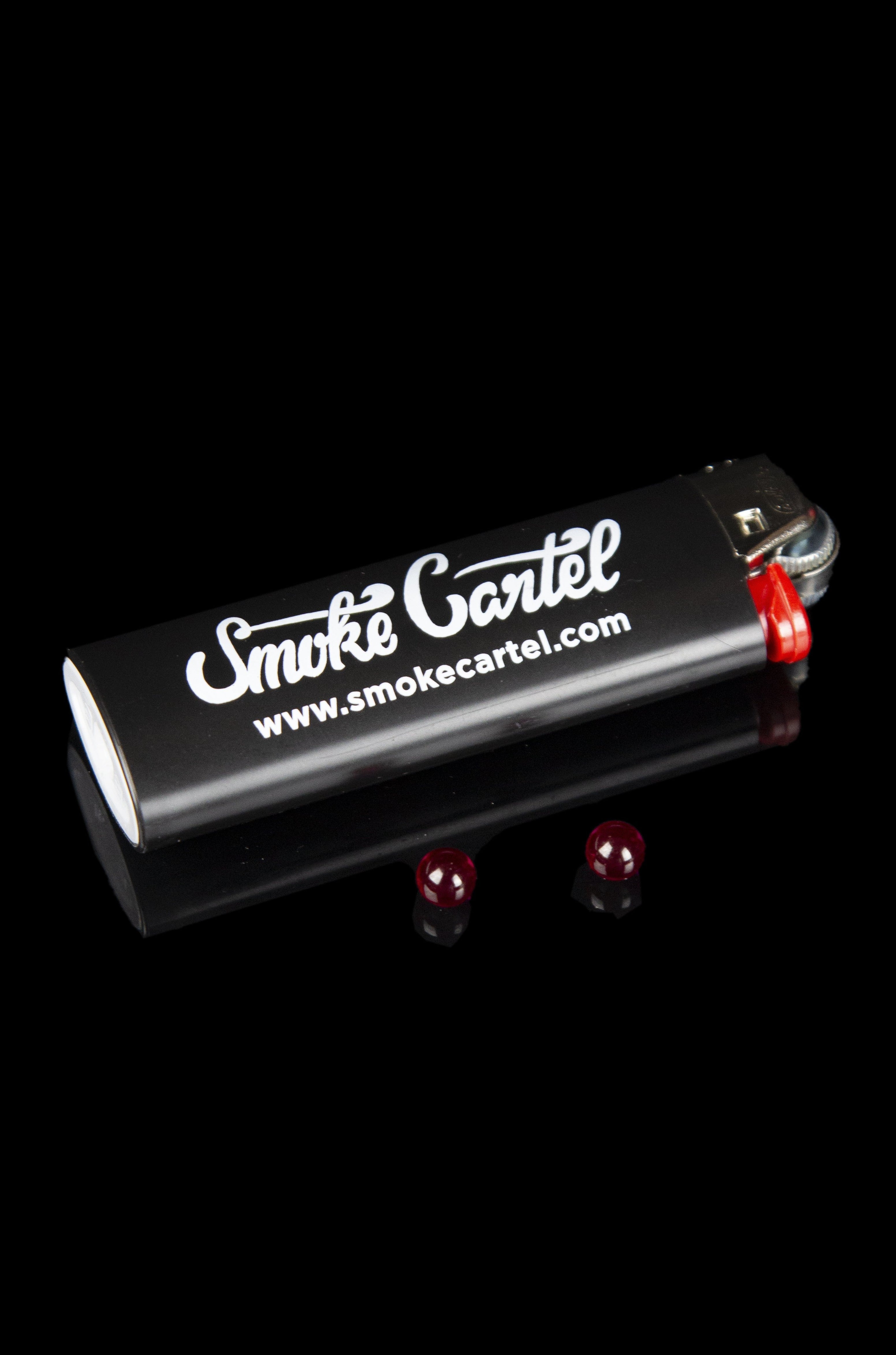 Black butane lighter with “Smoke Cartel” branding and red flame jets, isolated on a black background.