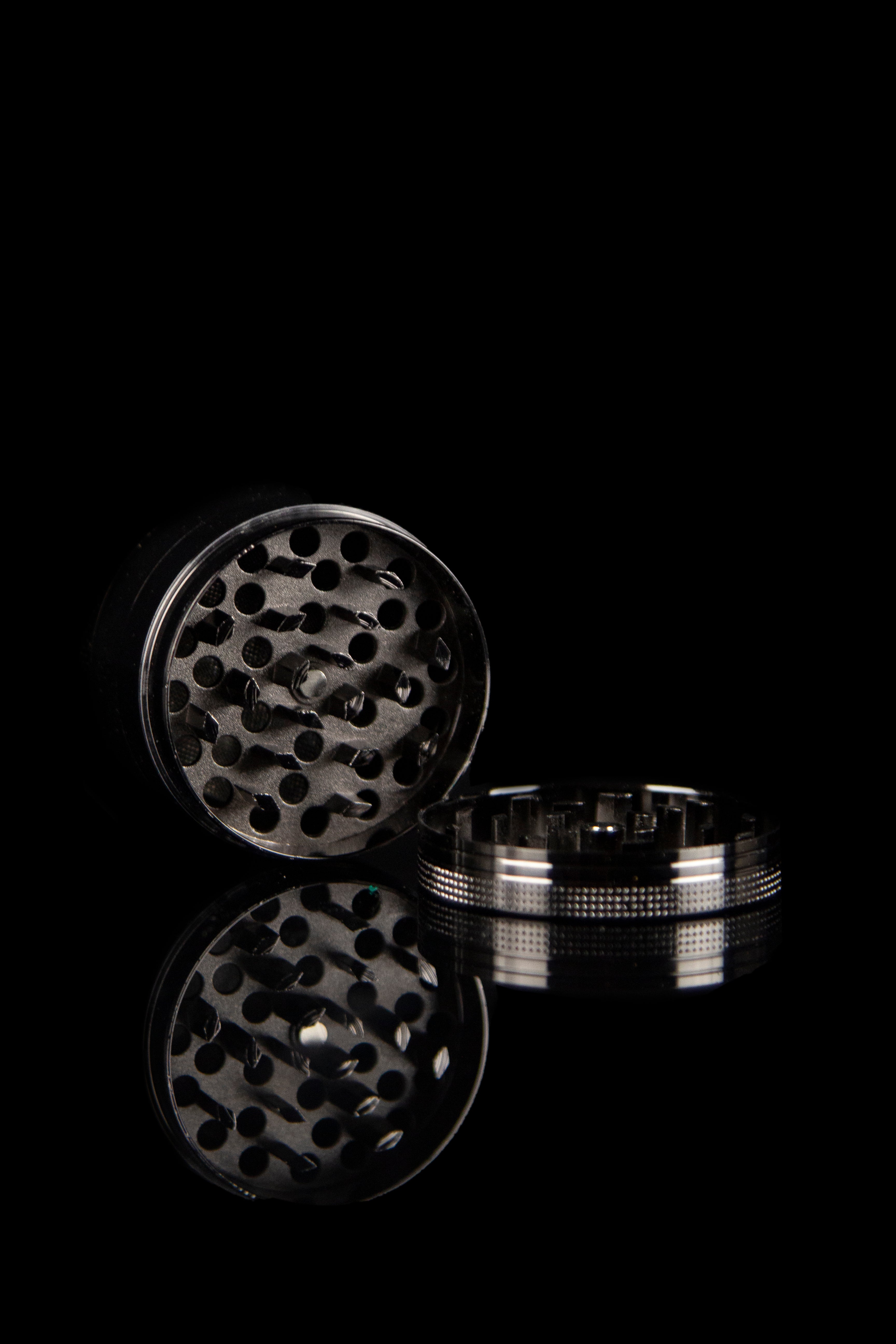 Open metal cannabis grinder against a black background.