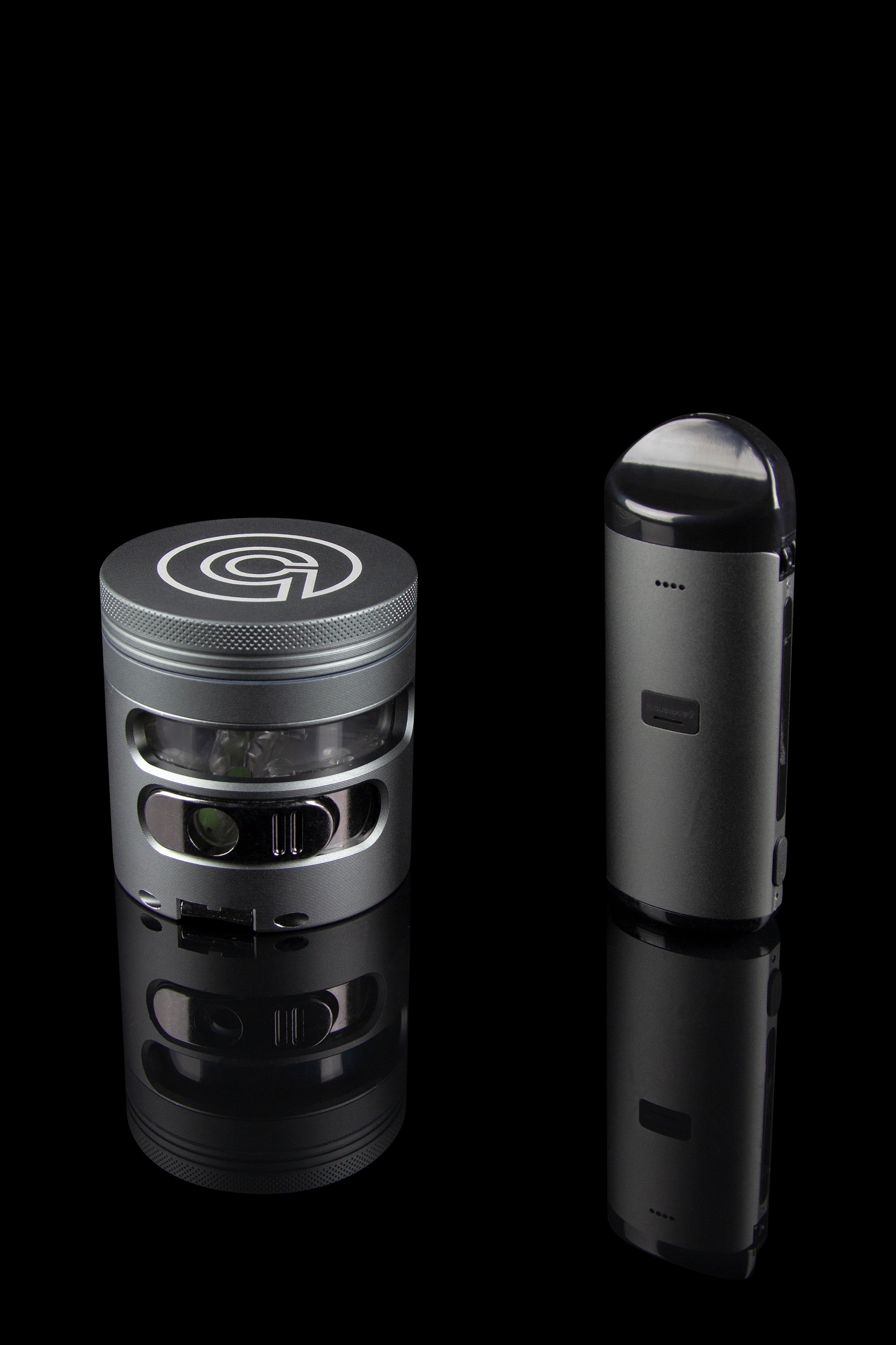 Sleek black cannabis grinder and vaporizer pen displayed on a reflective surface against a dark background.