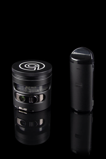 Black cannabis grinder and vaporizer pen displayed on a reflective surface.