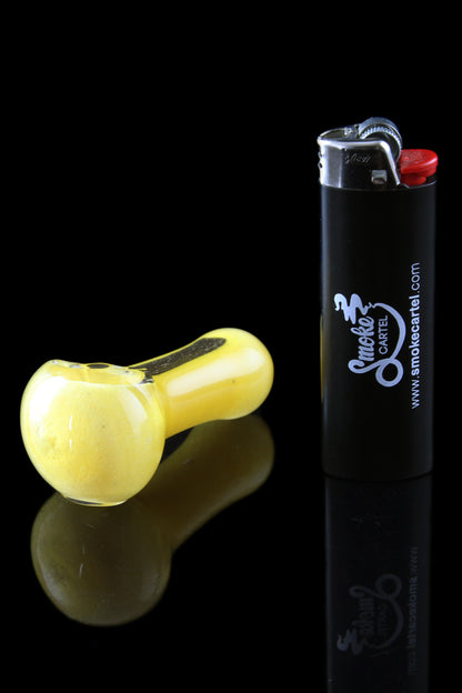 Yellow glass pipe and black lighter with “Smoke Cartel” branding on a reflective surface.