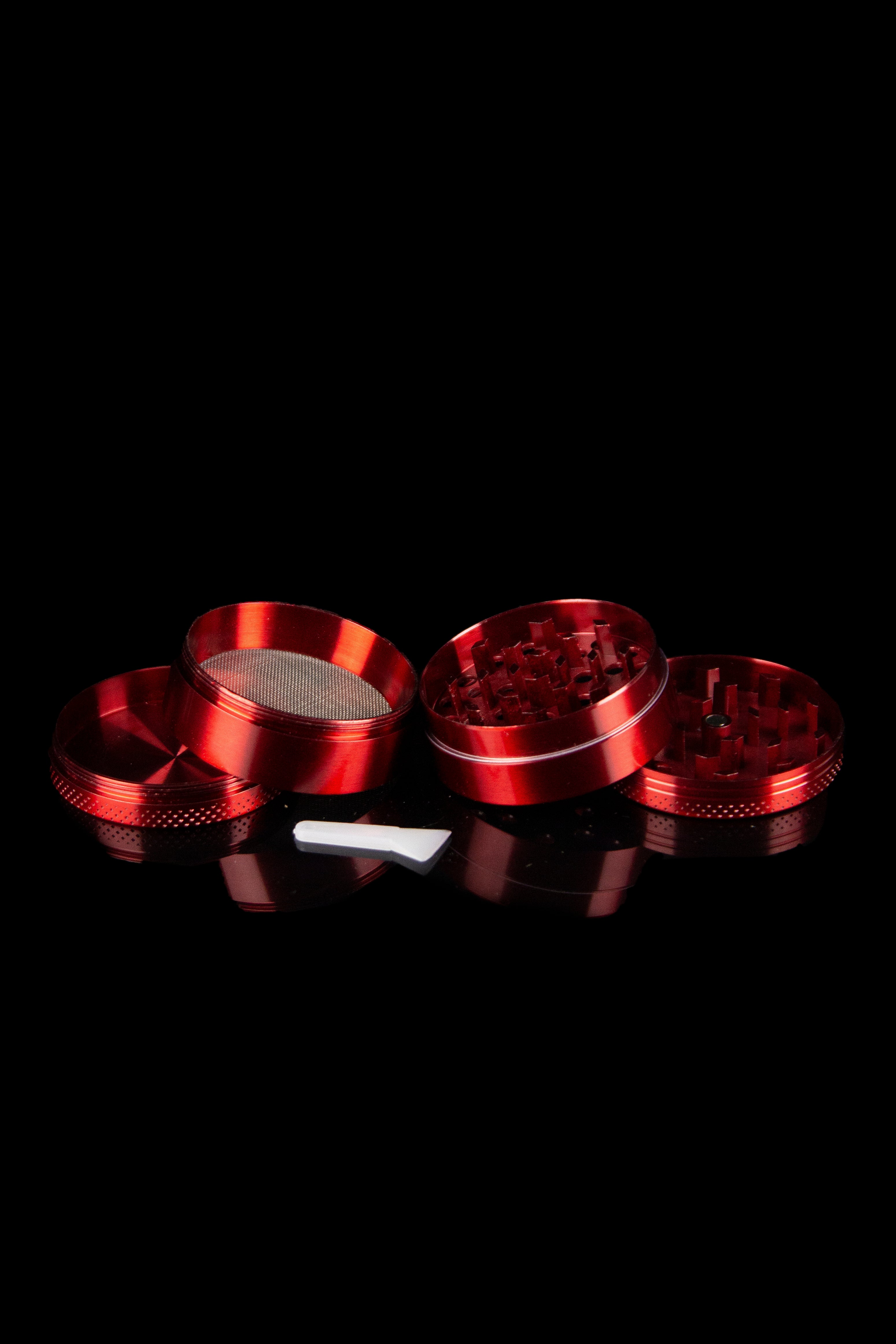 Red four-piece cannabis grinder with disassembled parts on a reflective black surface.