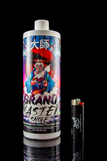 A bottle of “Grand Master Smoke” cleaning solution for pipes and bongs, positioned next to a lighter, against a dark reflective surface."