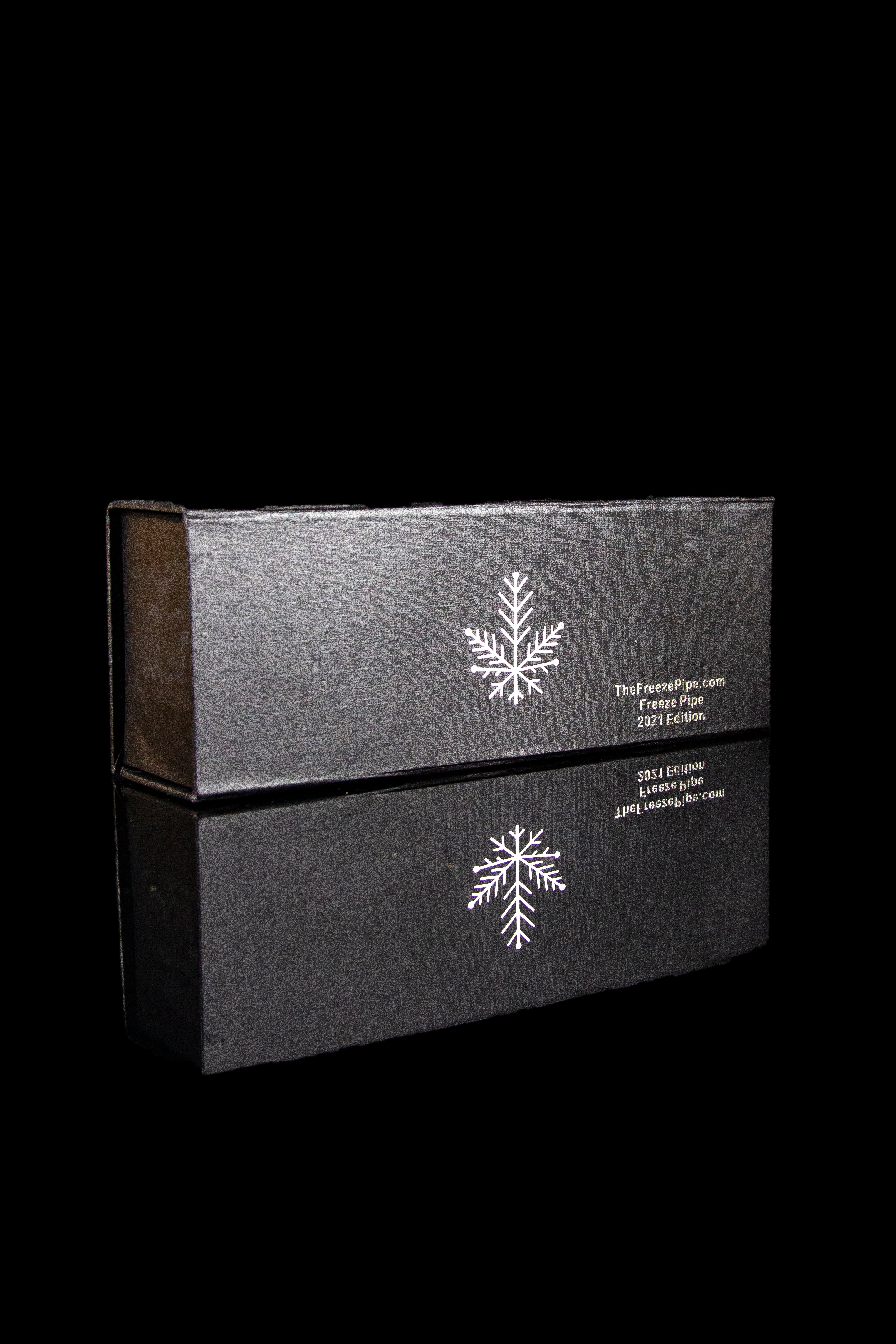 Black box with a snowflake design and cannabis accessory branding, reflected on a dark surface.