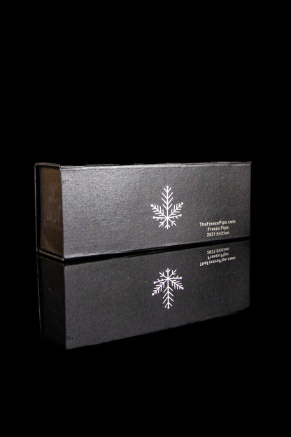 Black box with a snowflake design and cannabis accessory branding, reflected on a dark surface.
