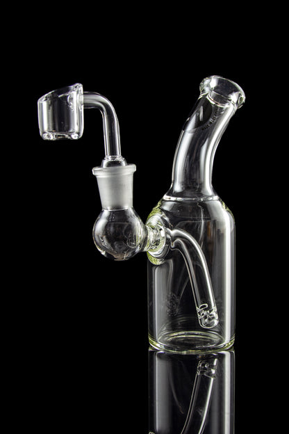 Clear glass dab rig with quartz banger, reflecting on a dark surface.