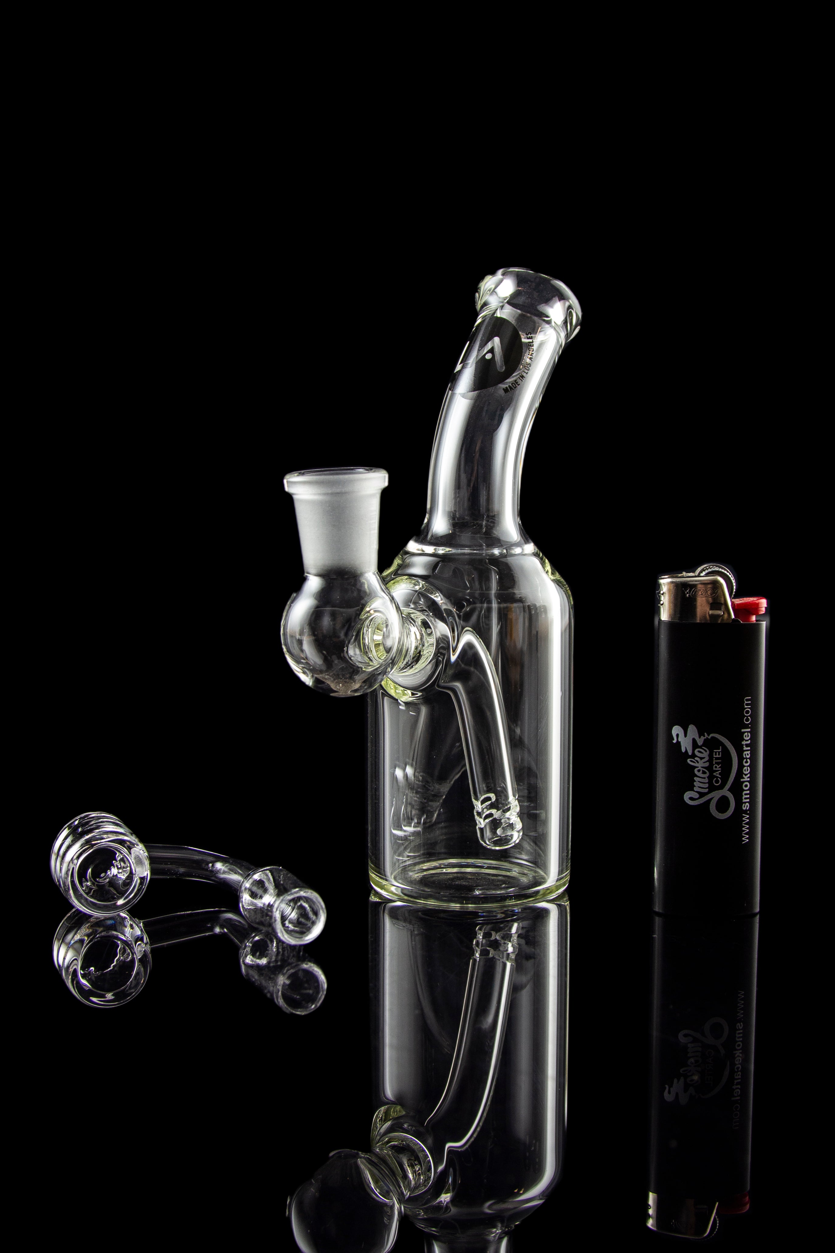 Clear glass water pipe (bong) with loose glass marbles and a lighter reflected on a glossy black surface.