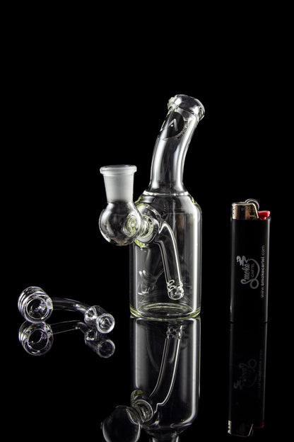 Clear glass water pipe (bong) with loose glass marbles and a lighter reflected on a glossy black surface.