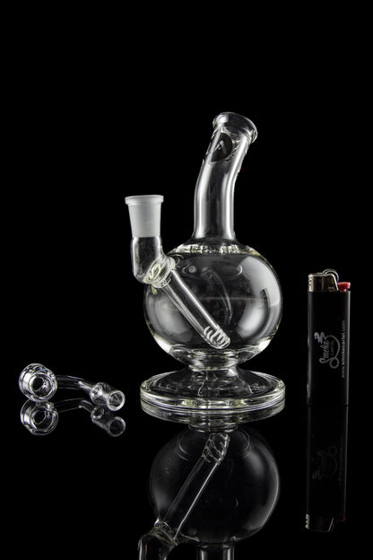 Clear glass water pipe (bubbler) with accompanying glass pieces and lighter, studio shot against a black background.