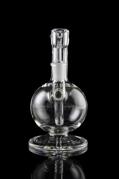 Clear glass water pipe (rig) with spherical body and intricate internal pathways, reflecting on a dark surface.