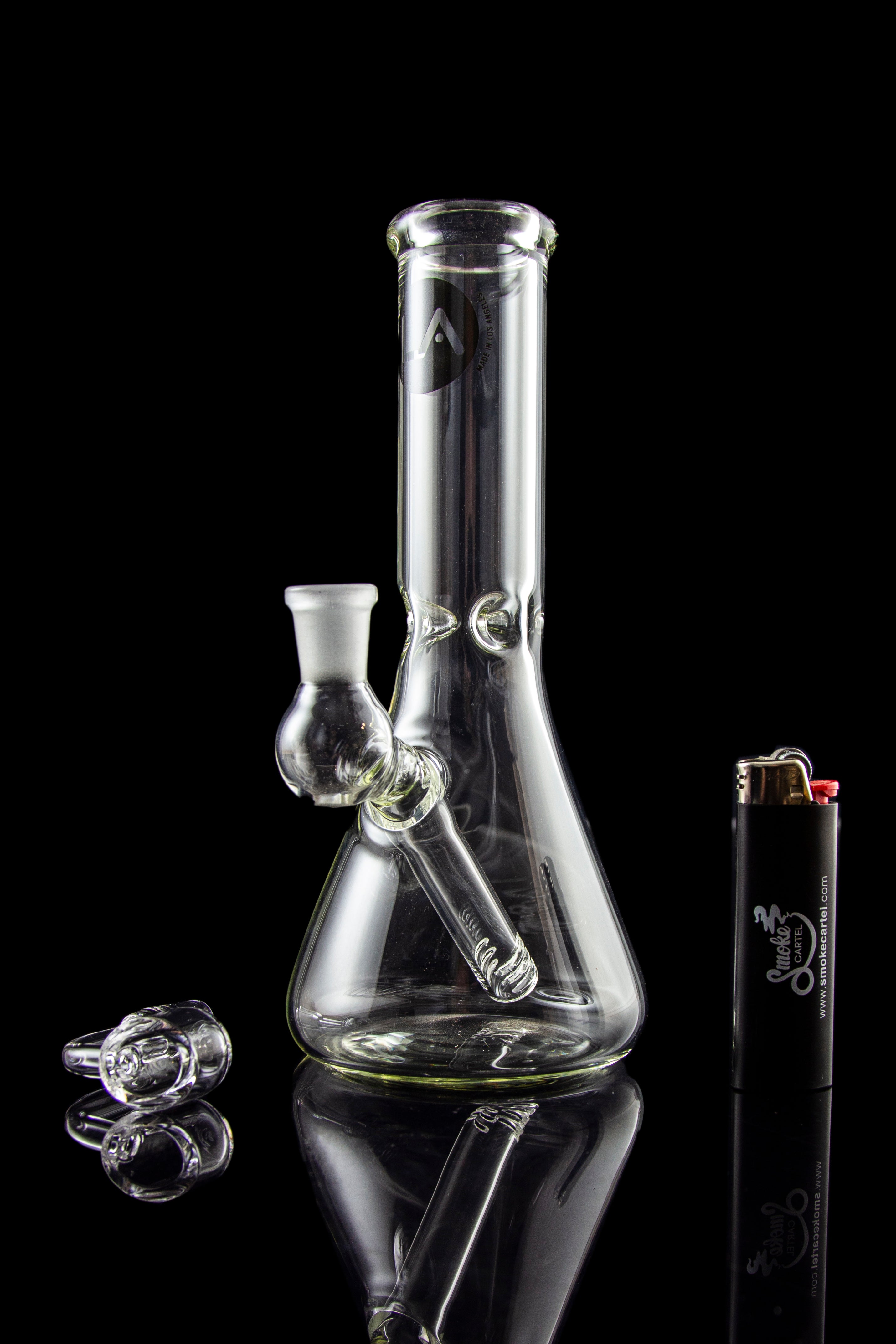 Glass bong and accessories on a reflective surface.