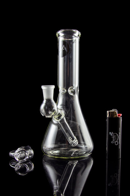 Glass bong and accessories on a reflective surface.