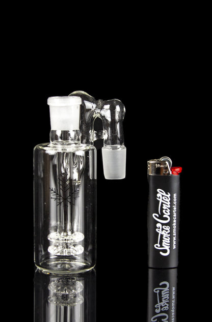 Glass bubbler with intricate design, reflecting on a black surface alongside a lighter branded with "Smoke Cartel".