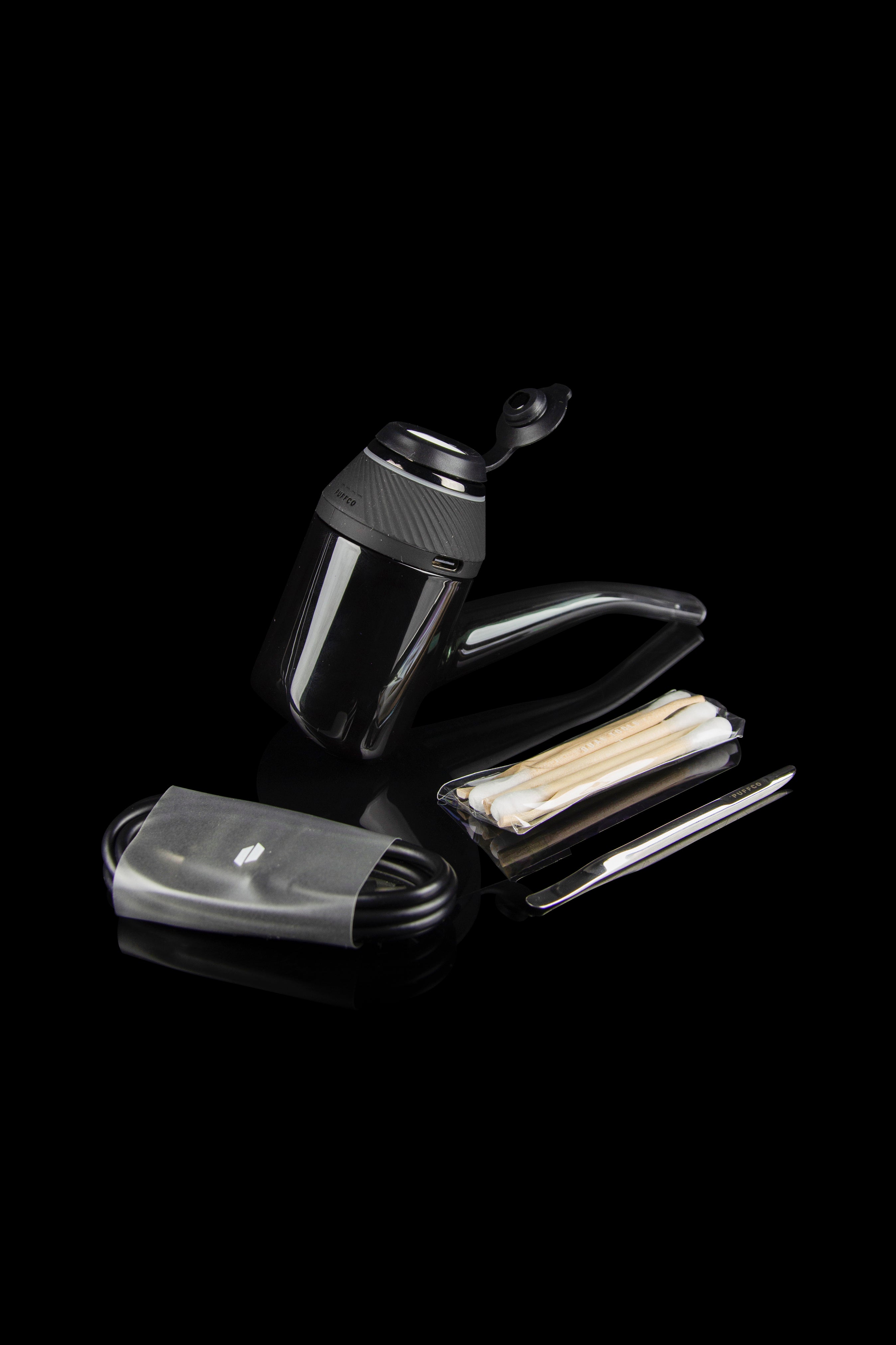 Black cannabis grinder, filter tips, and charging cable on a dark surface.