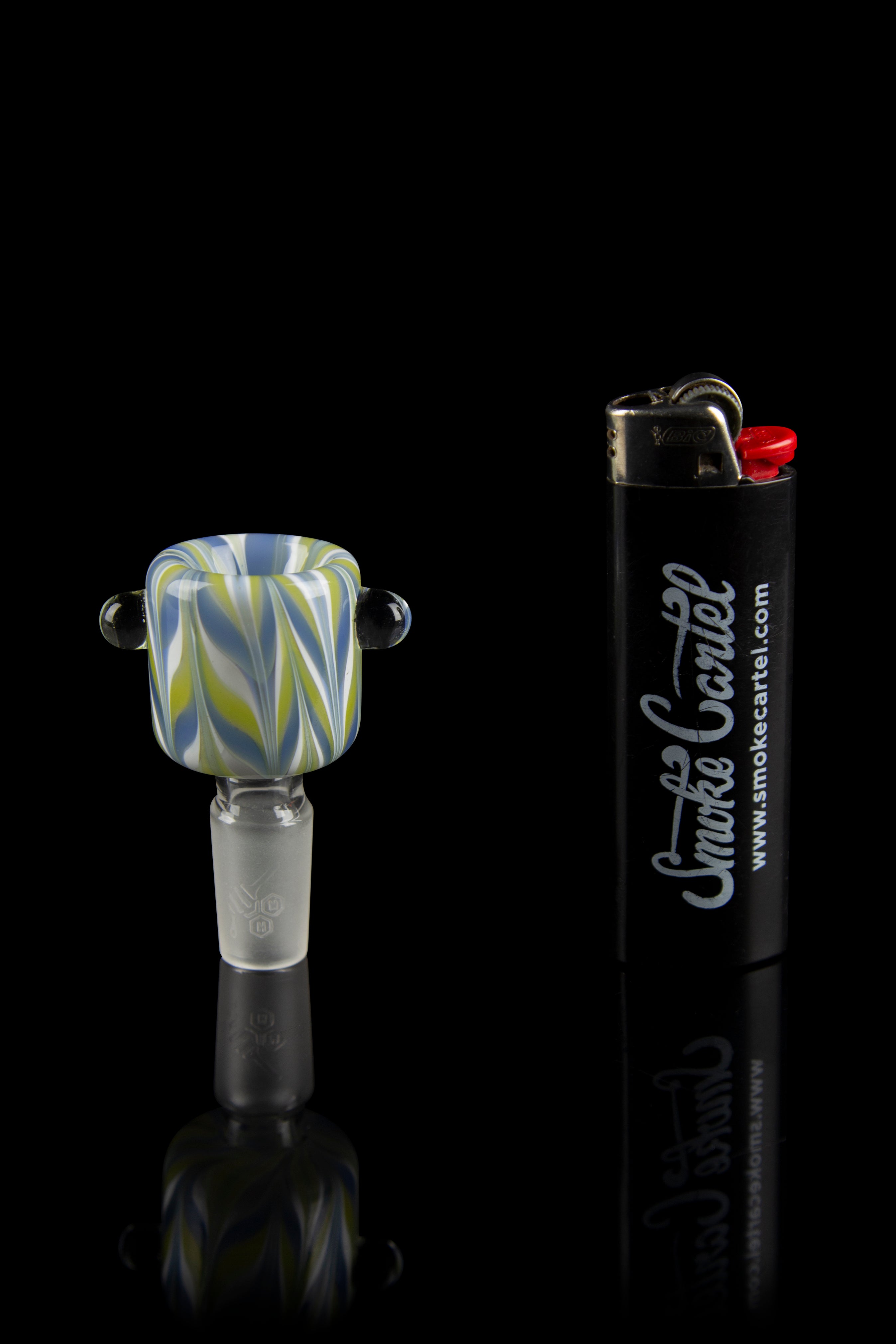 Close-up front view of the Honeybee Herb Wig Wag Flower Bowl showing its orange and black wig‑wag swirl and two small glass handles against a reflective black background